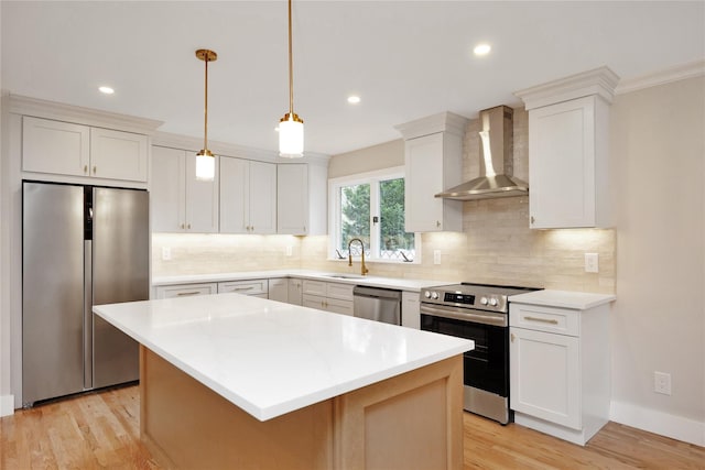 kitchen with stainless steel appliances, wall chimney range hood, a sink, light wood-style flooring, and a kitchen island