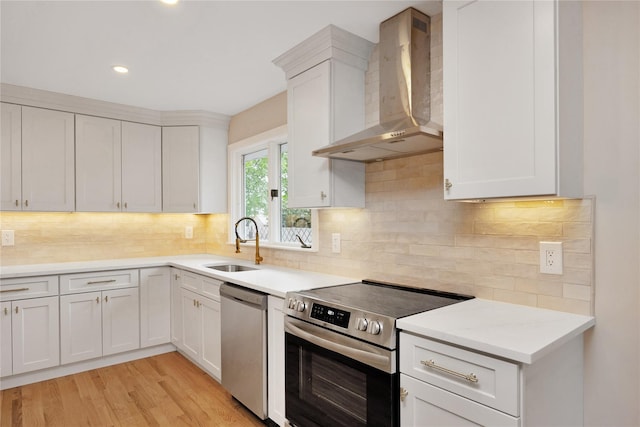 kitchen with wall chimney exhaust hood, stainless steel appliances, a sink, light countertops, and recessed lighting