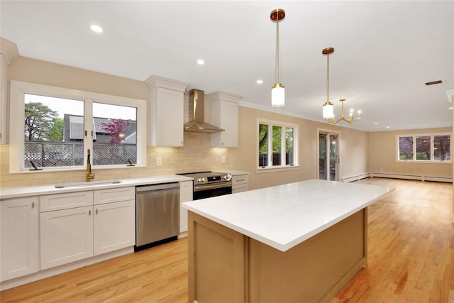 kitchen with appliances with stainless steel finishes, wall chimney exhaust hood, a sink, light wood-style floors, and a baseboard heating unit