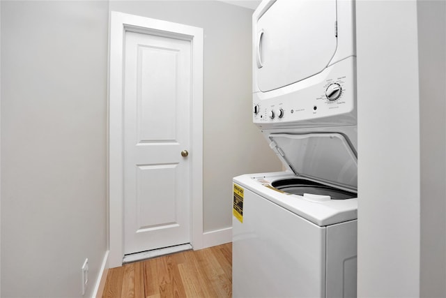 laundry area featuring stacked washer / drying machine, light wood finished floors, and baseboards