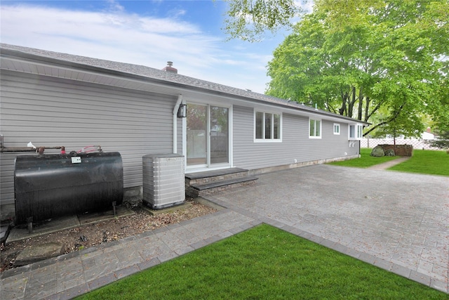 view of front of home with oil tank, central AC unit, a front yard, roof with shingles, and entry steps