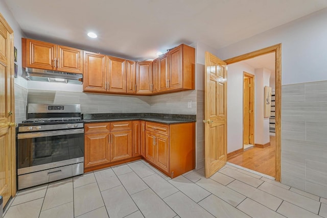 372 Grand Ave, Brooklyn, NY 11238 - kitchen featuring gas range, under cabinet range hood, light tile patterned floors, dark stone counters, and brown cabinetry
