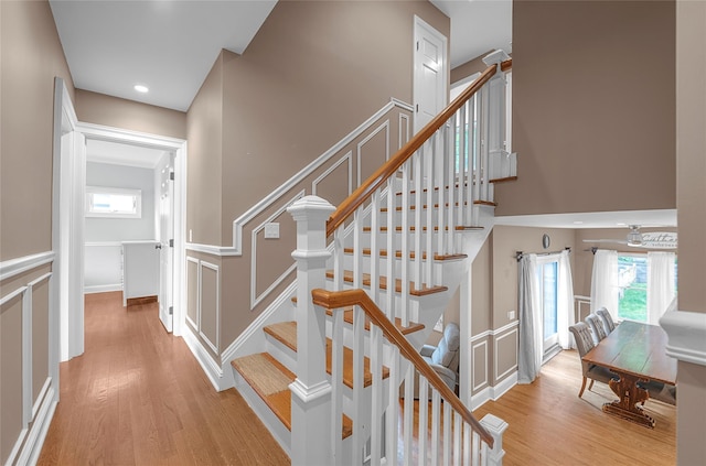 stairs with wood finished floors, plenty of natural light, a decorative wall, and recessed lighting