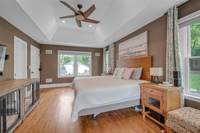 bedroom featuring wood finished floors, multiple windows, baseboards, a raised ceiling, and recessed lighting