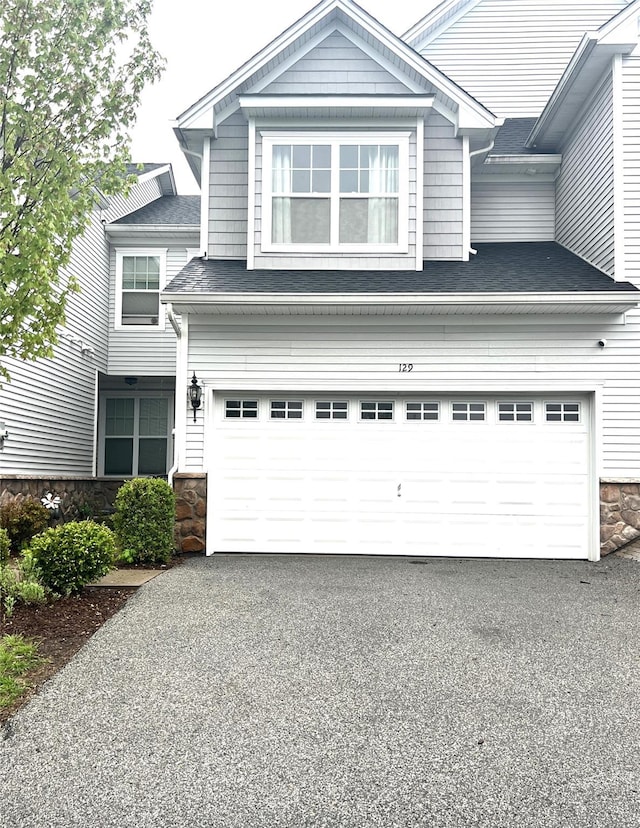 view of front of house featuring stone siding, roof with shingles, a garage, and driveway