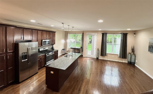 kitchen with a sink, light stone counters, dark brown cabinetry, baseboards, and appliances with stainless steel finishes