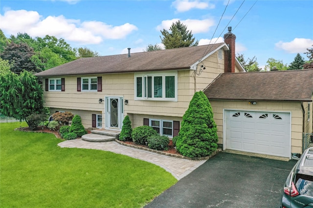 bi-level home with roof with shingles, a chimney, asphalt driveway, a garage, and a front yard