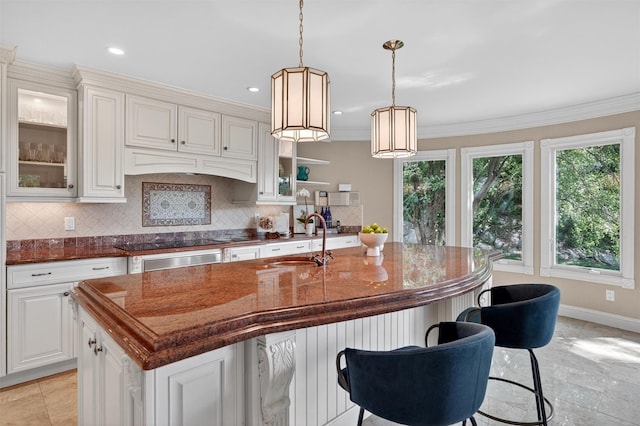 65 Round Hill Rd, Armonk, NY 10504 - kitchen featuring decorative backsplash, black electric stovetop, a center island with sink, a breakfast bar, and glass insert cabinets