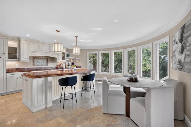 65 Round Hill Rd, Armonk, NY 10504 - kitchen featuring a kitchen island with sink, a breakfast bar, decorative backsplash, glass insert cabinets, and ornamental molding