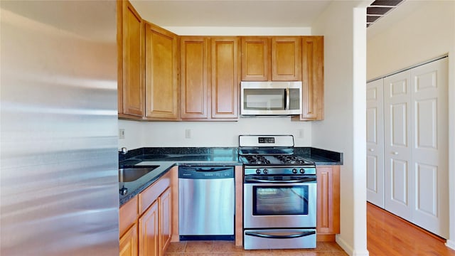 6910 Beach Front Rd, Arverne, NY 11692 - kitchen with stainless steel appliances, a sink, brown cabinetry, and dark stone counters