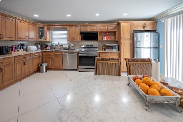 kitchen with a sink, brown cabinetry, stainless steel appliances, decorative backsplash, and light stone countertops