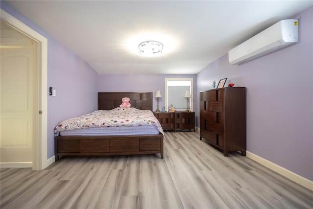 bedroom featuring light wood-style flooring, an AC wall unit, and baseboards