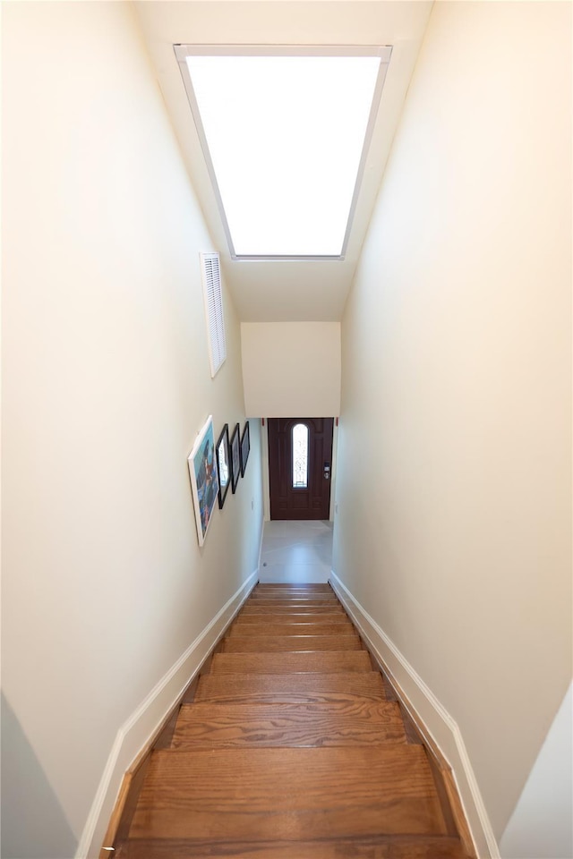 staircase with baseboards, a skylight, and wood finished floors