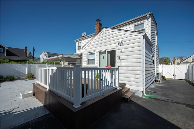 rear view of property with a gate, a chimney, a wooden deck, and a fenced backyard
