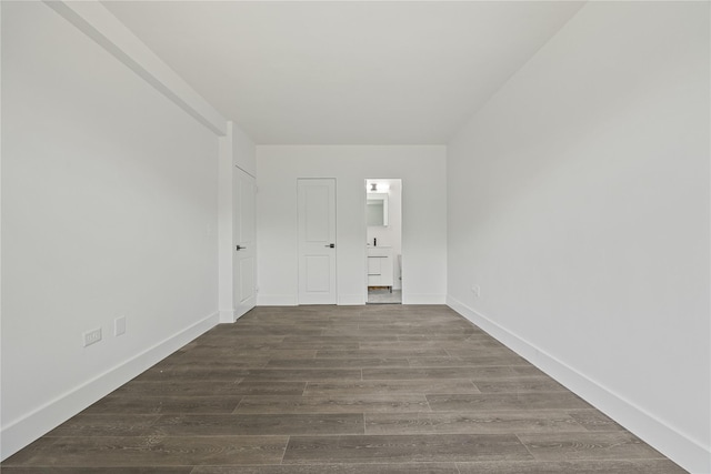 unfurnished bedroom featuring dark wood-style flooring, connected bathroom, and baseboards