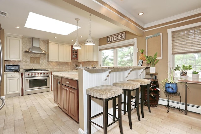 kitchen with wall chimney range hood, high end range, a skylight, a breakfast bar area, and tasteful backsplash