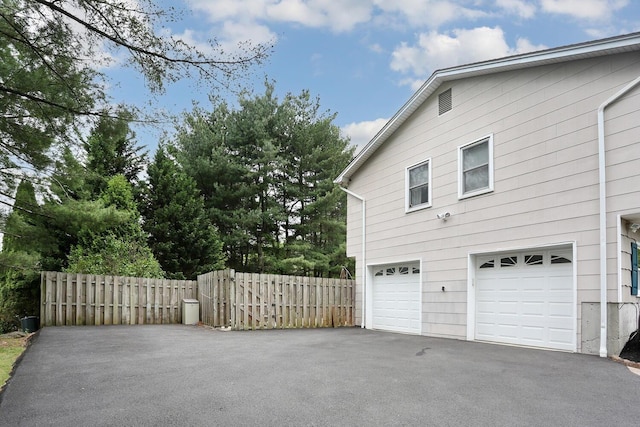 view of home's exterior featuring asphalt driveway, an attached garage, and fence