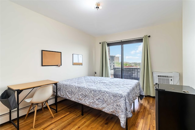 bedroom with wood finished floors, a wall mounted air conditioner, baseboard heating, and access to outside
