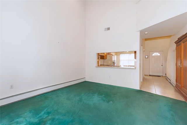 unfurnished living room featuring baseboard heating, light colored carpet, a high ceiling, light tile patterned floors, and a baseboard heating unit