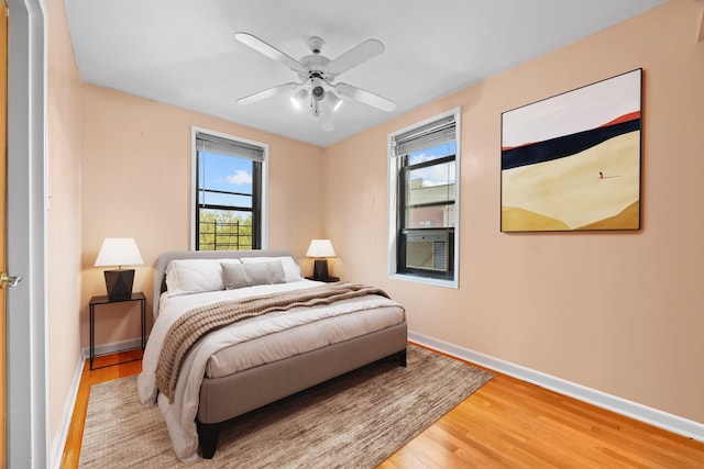 bedroom featuring light wood-style flooring, baseboards, ceiling fan, and cooling unit