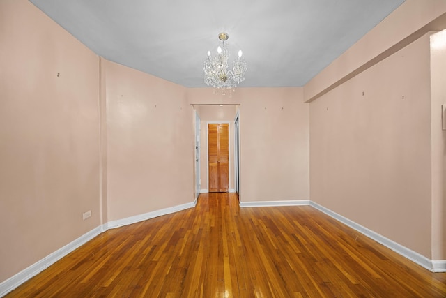 spare room featuring a chandelier, hardwood / wood-style flooring, and baseboards