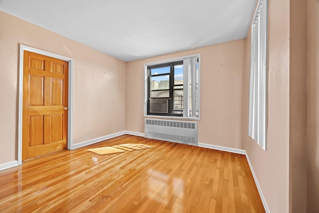 unfurnished room with radiator heating unit, light wood finished floors, and baseboards