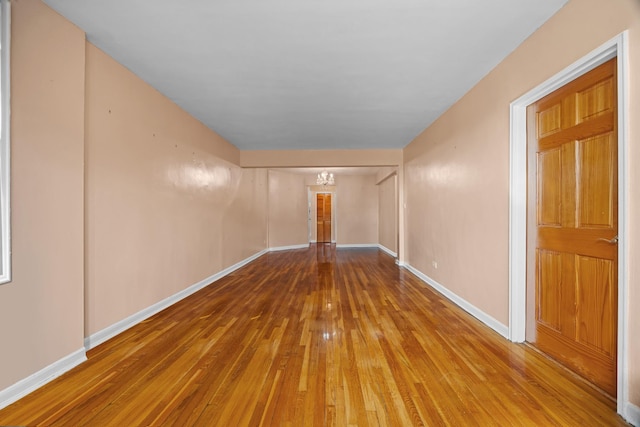 empty room featuring a chandelier, wood-type flooring, and baseboards