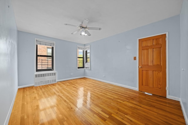 unfurnished room featuring radiator, light wood-style floors, baseboards, ceiling fan, and cooling unit