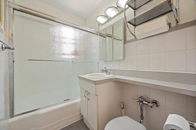 bathroom with toilet, vanity, shower / bath combination with glass door, tasteful backsplash, and tile walls