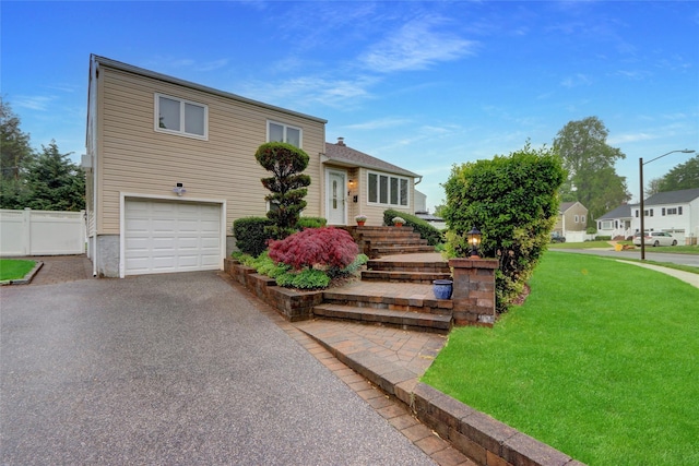split level home featuring a front yard, fence, a garage, and aphalt driveway