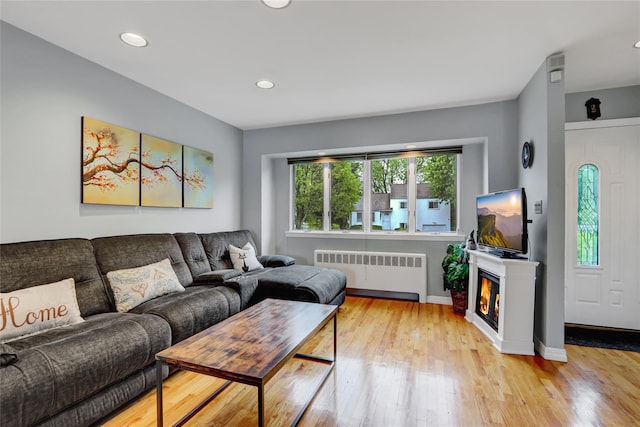 living room featuring radiator heating unit, recessed lighting, light wood finished floors, a lit fireplace, and baseboards