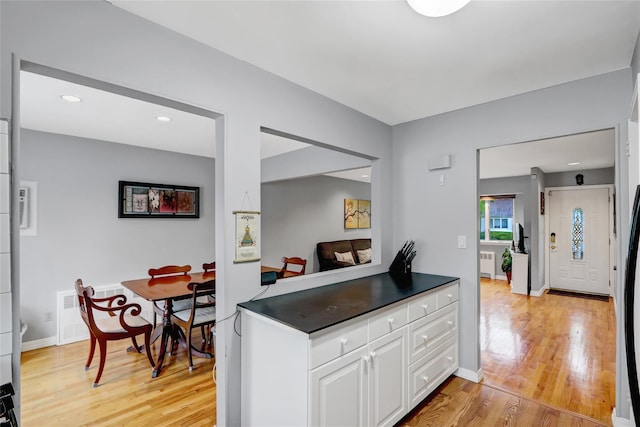 kitchen featuring light wood-style flooring, dark countertops, white cabinetry, visible vents, and radiator heating unit