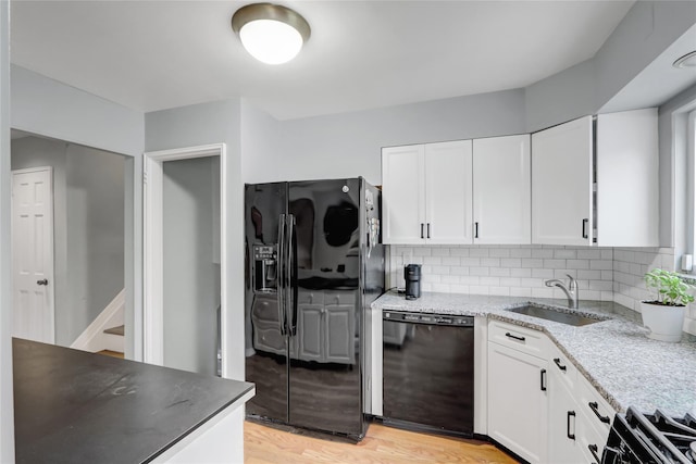 kitchen featuring a sink, light stone counters, black appliances, backsplash, and white cabinetry