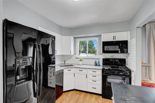 kitchen featuring light wood finished floors, a sink, white cabinetry, black appliances, and backsplash