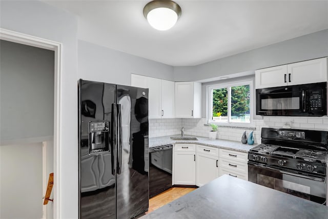kitchen featuring white cabinetry, black appliances, light wood-style flooring, and backsplash