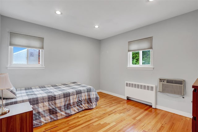 bedroom featuring radiator heating unit, recessed lighting, a wall mounted AC, baseboards, and light wood-style floors