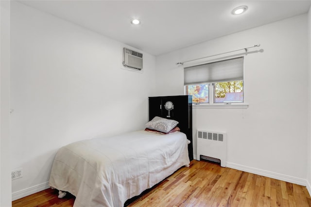 bedroom with light wood-style flooring, recessed lighting, a wall unit AC, baseboards, and radiator heating unit