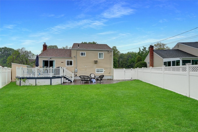 back of house featuring a fenced backyard, a wooden deck, a chimney, and a lawn