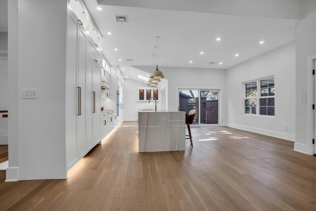 kitchen with light wood finished floors, a kitchen island with sink, white cabinetry, recessed lighting, and a kitchen breakfast bar