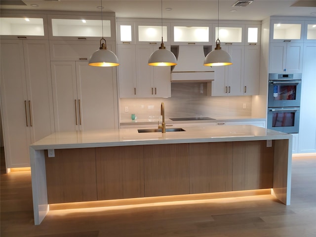 kitchen with a sink, multiple ovens, custom exhaust hood, and light countertops