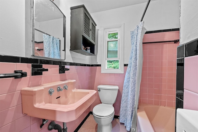 bathroom with toilet, tile walls, a wainscoted wall, shower / bath combo with shower curtain, and a sink