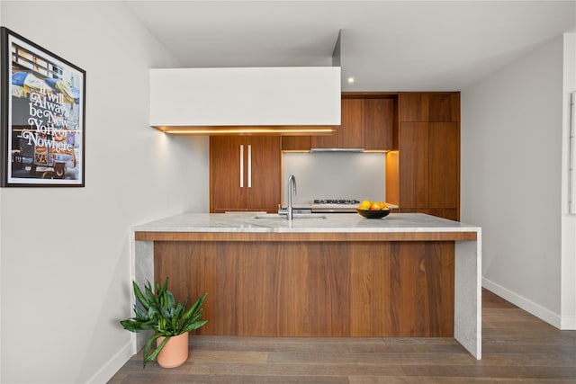 kitchen featuring brown cabinetry, baseboards, modern cabinets, a sink, and a peninsula