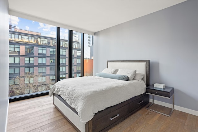 bedroom featuring floor to ceiling windows, wood finished floors, and baseboards