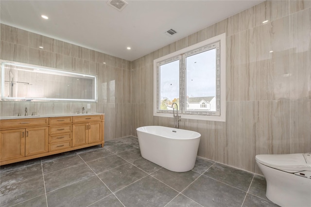 bathroom featuring a sink, tile walls, visible vents, and a freestanding tub