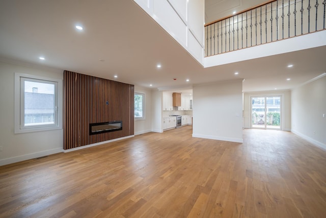 396 Argyle Rd, East Meadow, NY 11554 - unfurnished living room with plenty of natural light, crown molding, light wood finished floors, a glass covered fireplace, and baseboards