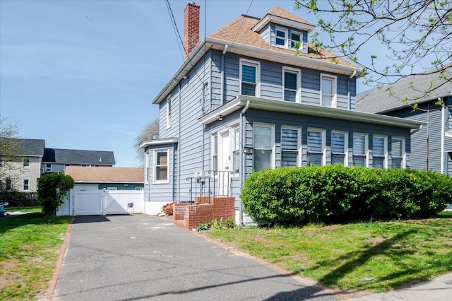 traditional style home featuring a chimney, a front lawn, and a gate