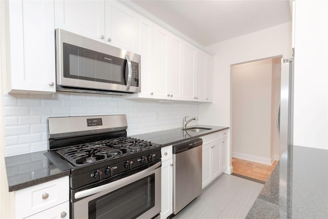 kitchen featuring appliances with stainless steel finishes, a sink, decorative backsplash, dark stone countertops, and white cabinetry