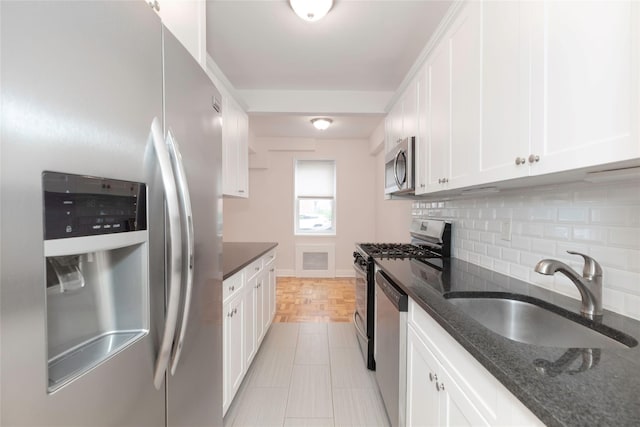 kitchen featuring stainless steel appliances, a sink, decorative backsplash, white cabinetry, and dark stone counters