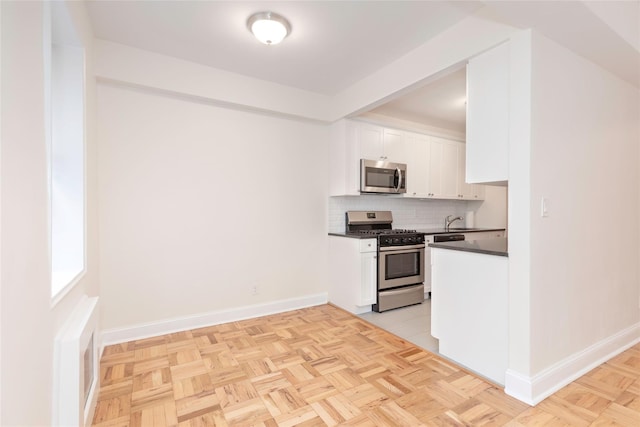 kitchen with appliances with stainless steel finishes, tasteful backsplash, white cabinets, dark countertops, and baseboards