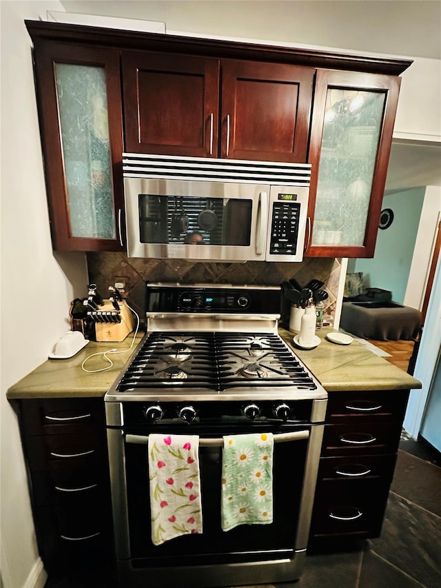 kitchen featuring stainless steel microwave, gas stove, light countertops, decorative backsplash, and glass insert cabinets